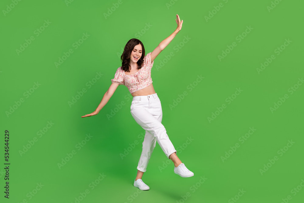 Full size photo of cute pretty cheerful woman with wavy hairstyle wear white trousers top flying isolated on green color background Full size photo of cute pretty cheerful woman with wavy hairstyle wear white trousers top flying isolated on green color background