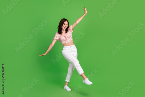 Full size photo of cute pretty cheerful woman with wavy hairstyle wear white trousers top flying isolated on green color background © deagreez