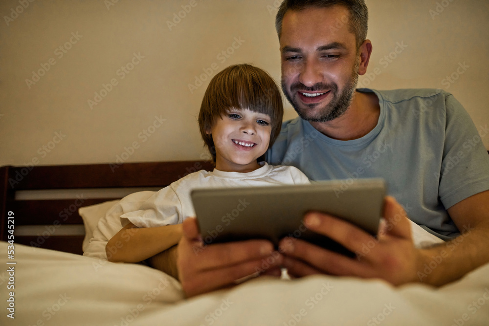 Smiling father and son watch digital tablet in bed Smiling father and son watch digital tablet in bed