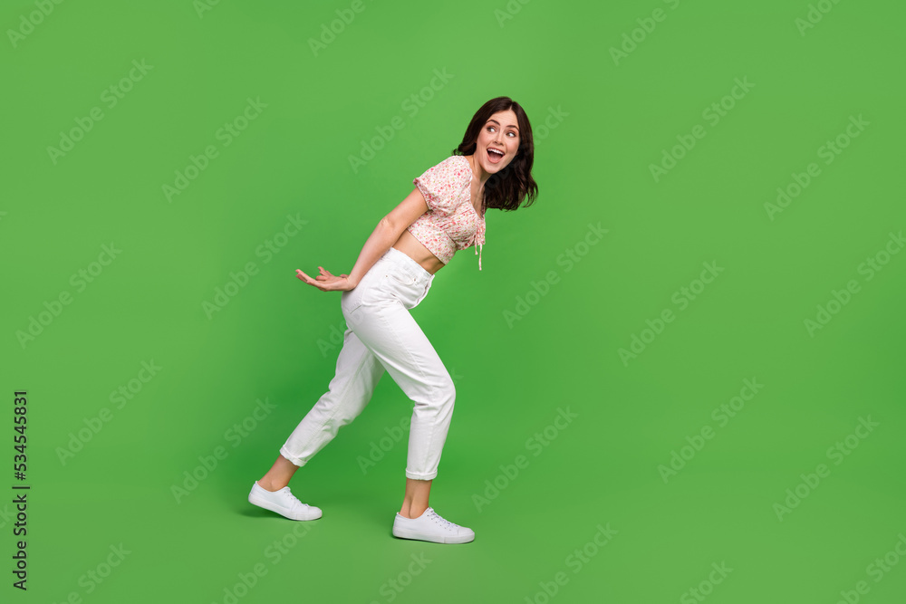 Full size photo of excited lovely girl curly hairstyle dressed white pants blouse drag look empty space isolated on green color background Full size photo of excited lovely girl curly hairstyle dressed white pants blouse drag look empty space isolated on green color background