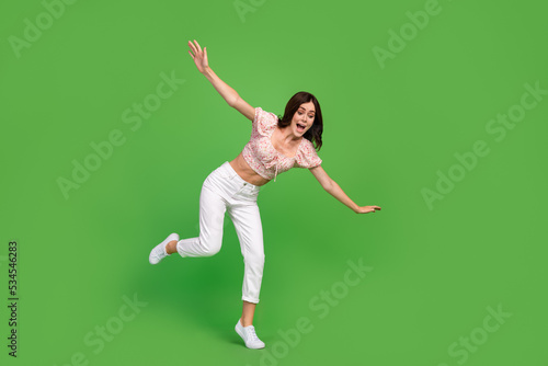 Full size photo of lovely positive woman with wavy hairstyle dressed white pants blouse look down fall isolated on green color background