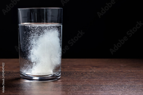 Effervescent tablet in a glass of water close-up on a black background. The concept of health. photo