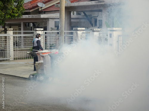 MELAKA, MALAYSIA - JUNE 1, 2022: The fogging of mosquito repellent is being carried out using a special machine. Spray workers need to wear a special face mask to avoid smelling the poison.