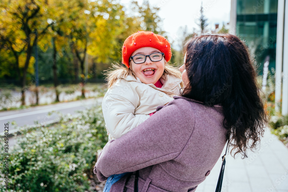 Fototapeta premium Cute little girl in a red beret with special needs enjoy having fun spending time with mother outdoor in aututm time. Happy family moments concept.