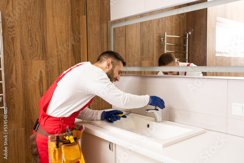 Professional plumber, male worker in uniform installing sink and water pipe in new apartment