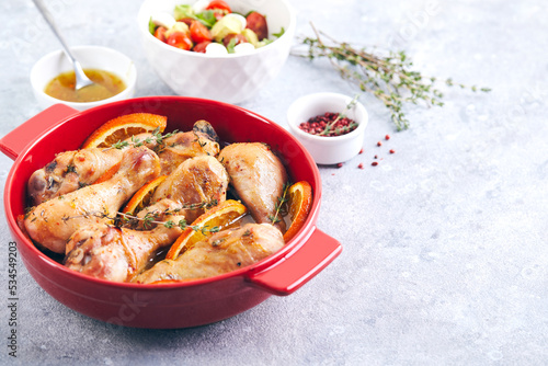 Chicken drumsticks with oranges and thyme baked in red round baking dish