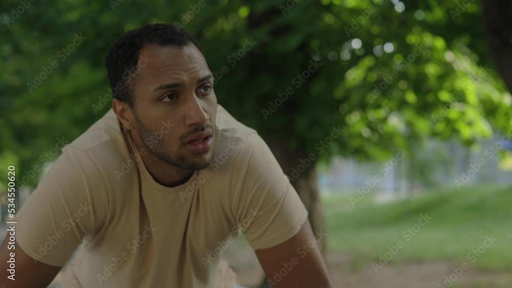 Close view of the of the african american runner stopping to take deep breath during the training in the park wearing the smart watch. Blurred park background. Sport and healthy lifestyle concept. Close view of the of the african american runner stopping to take deep breath during the training in the park wearing the smart watch. Blurred park background. Sport and healthy lifestyle concept.