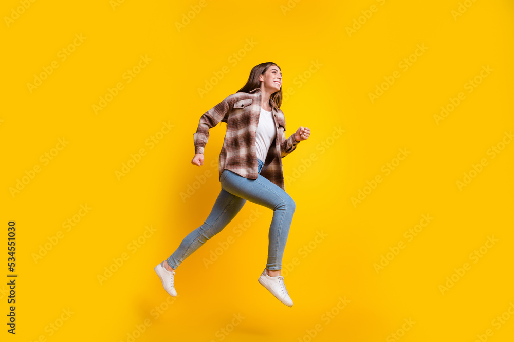 Full length photo of shiny pretty lady wear checkered shirt jumping high hurrying empty space isolated yellow color background