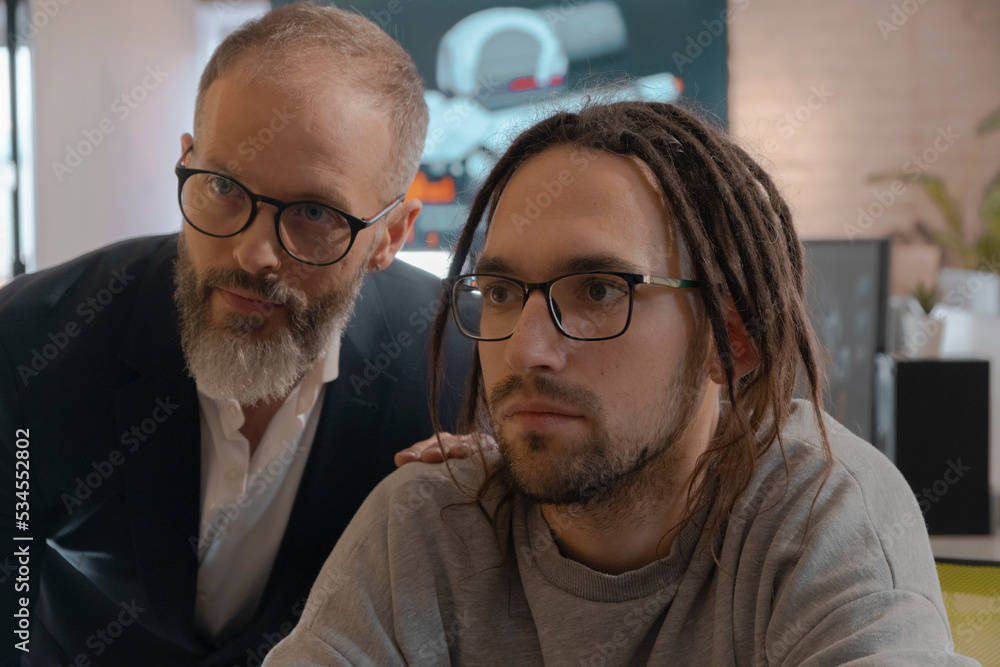 CEO of company and European man discusses something and looks at monitor in an office for the development of games and computer applications. CEO of company and European man discusses something and looks at monitor in an office for the development of games and computer applications.