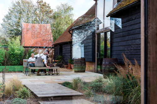 Family sitting at bench outside countryside house.