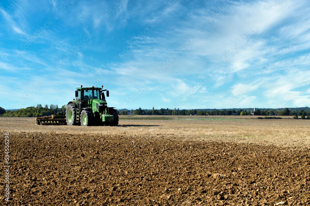 Fototapeta premium An agricultural tractor working in a plowed field during the autumn season