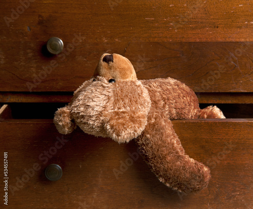 A children's brown soft toy teddy bear hanging out of a drawer. photo