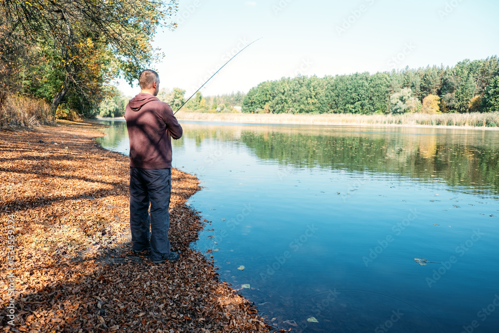 Fisherman with spinning rod on the autumn lake. fisherman with spinning in his hands catching fish at sun day. Fisherman with rod, spinning reel on the river bank. Fisherman with spinning rod on the autumn lake. fisherman with spinning in his hands catching fish at sun day. Fisherman with rod, spinning reel on the river bank.