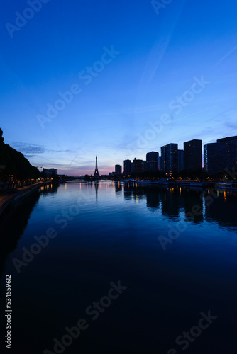 A view along the water of the River Seine at night, tall buildings on the river bank, the Eiffel tower in the distance. photo