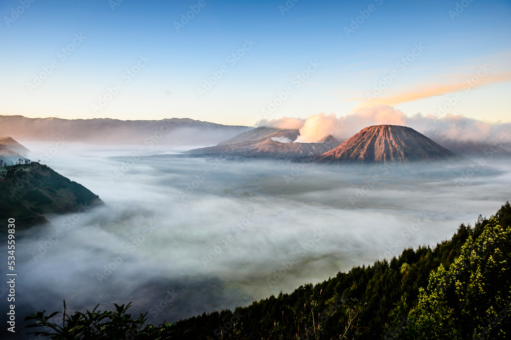 Mount Bromo volcano, a somma volcano and part of the Tengger mountains range, the cone rising above mist in the landscape. Mount Bromo volcano, a somma volcano and part of the Tengger mountains range, the cone rising above mist in the landscape.