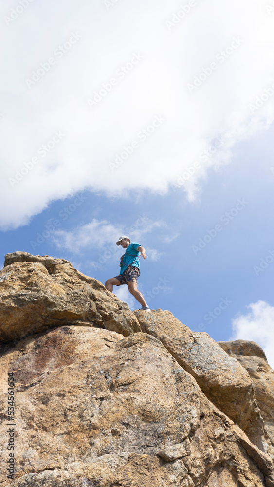 low view of man walking on a rock cliff with blue sky in background . copy space