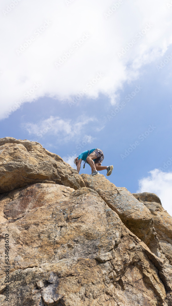 low view of man climbing on rock with blue sky in background . copy space