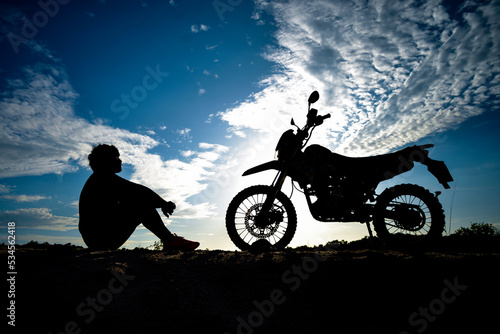 Silhouette of a lonely, heartbroken, disappointed man having a motocross bike on the mountain in a beautiful evening. Broken hearted, disappointed and lonely concept. © STOCK PHOTO 4 U