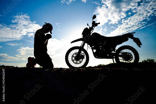 Silhouette of a lonely  heartbroken  disappointed man having a motocross bike on the mountain in a beautiful evening. Broken hearted  disappointed and lonely concept.