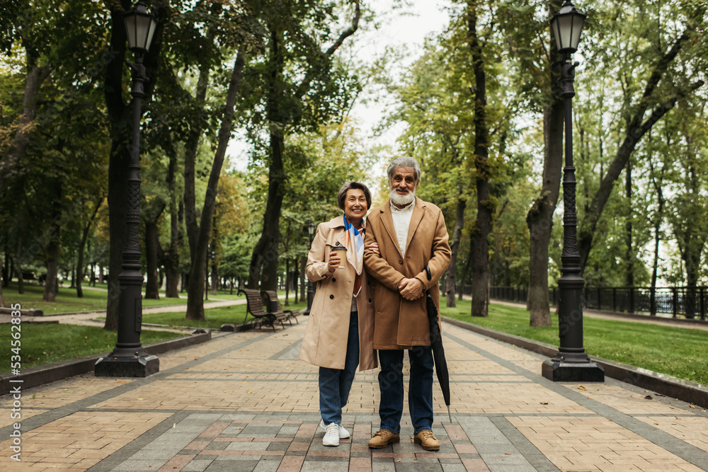 full length of senior woman holding paper cup while standing with stylish husband in coat. full length of senior woman holding paper cup while standing with stylish husband in coat.