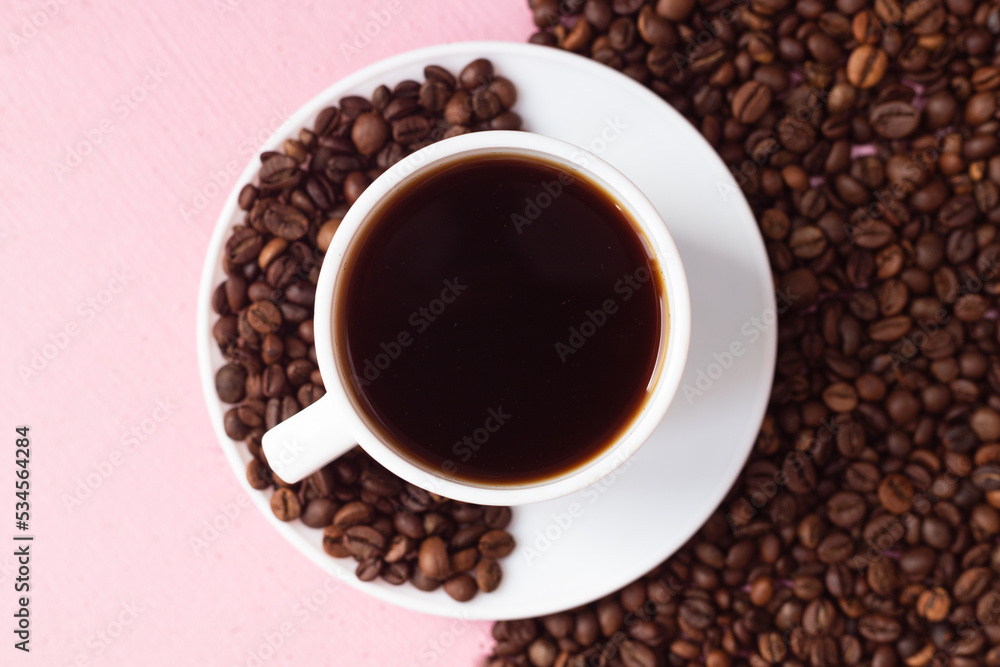 A mug with black coffee on a pink background. Half of the background is lined with coffee beans A mug with black coffee on a pink background. Half of the background is lined with coffee beans