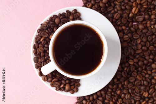 A mug with black coffee on a pink background. Half of the background is lined with coffee beans