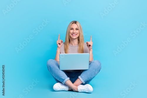 Full length photo of sweet funny lady wear grey sweatshirt typing modern gadget pointing up empty space isolated blue color background © deagreez