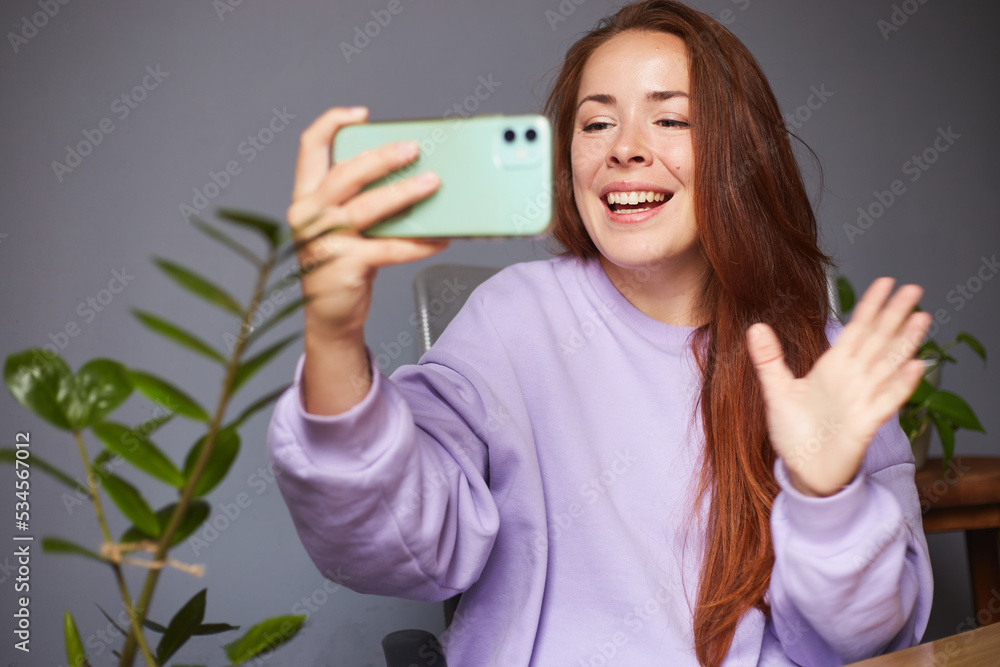 Cheerful caucasian female making selfie. A lot of green plants around. Red hair woman in violet sweater Cheerful caucasian female making selfie. A lot of green plants around. Red hair woman in violet sweater