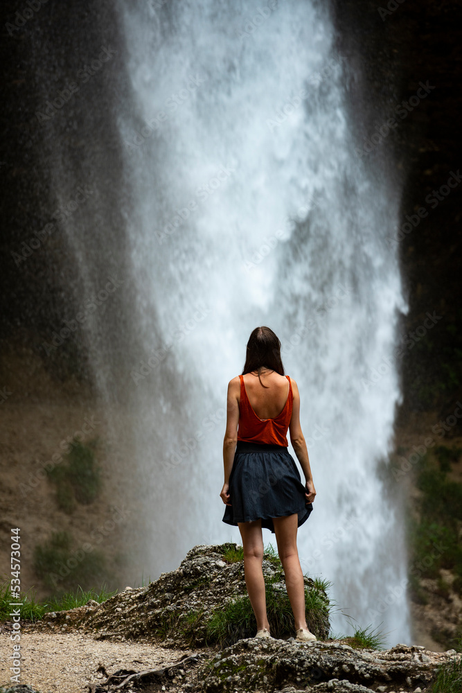 Obraz premium beautiful woman in blue skirt standing in front of large waterfall in slovenia, closeup photography of pretty woman with huge waterfall in the background (Peričnik)