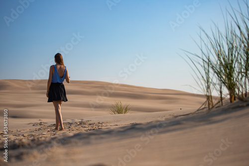 young long-haired woman with huge dunes and sandy hills in the background; woman lost in the desert