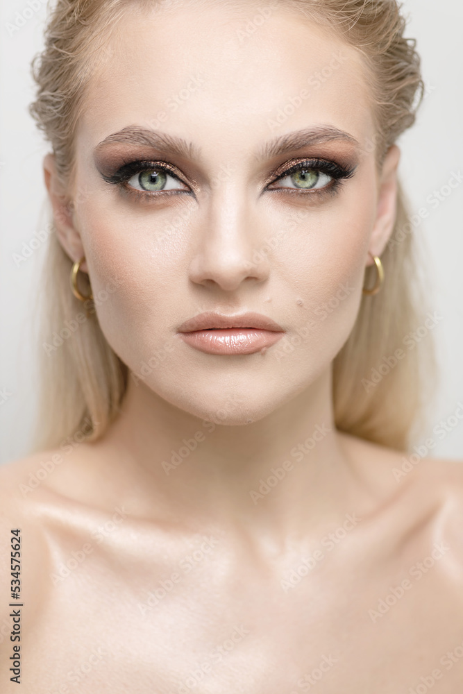 Fashion and make-up concept. Beautiful blonde girl with green eyes studio portrait. Sexy looking model with fancy evening make-up looking to camera. Eyes is in focus. Toned image with beige color