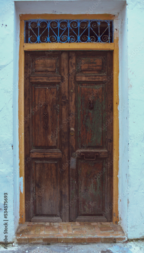 Vieja puerta de tablas de madera de entrada de una casa con reja en la parte superior.