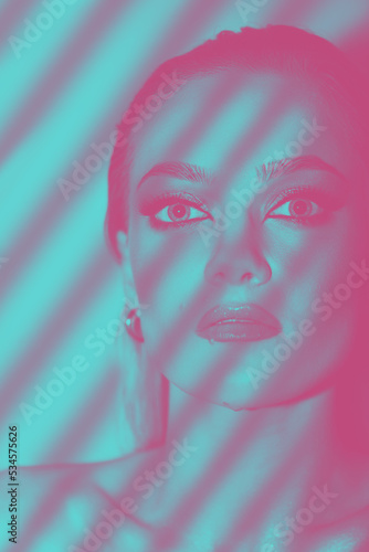 Fototapeta Naklejka Na Ścianę i Meble -  Beautiful girl studio portrait. Sexy looking woman with fancy evening makeup looking to camera. Blinds shadow casts on model face. Eyes is in focus. Purple and blue vivid color gradient map applied