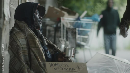 African American man giving donation to homeless beggar on street and supporting him with kind words
