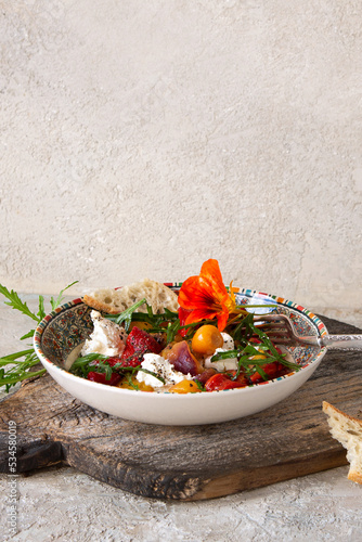 a bowl of salad with baked peppers, tomatoes and soft cheese on the table