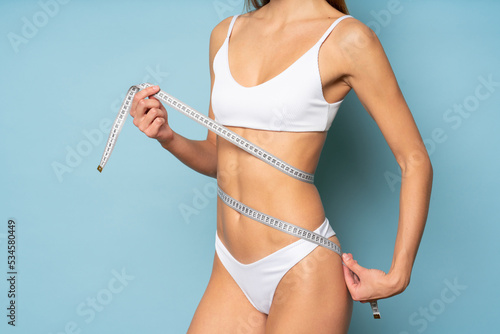 Woman in bikini with no face doing measurements of body size with measuring tape around waist photo