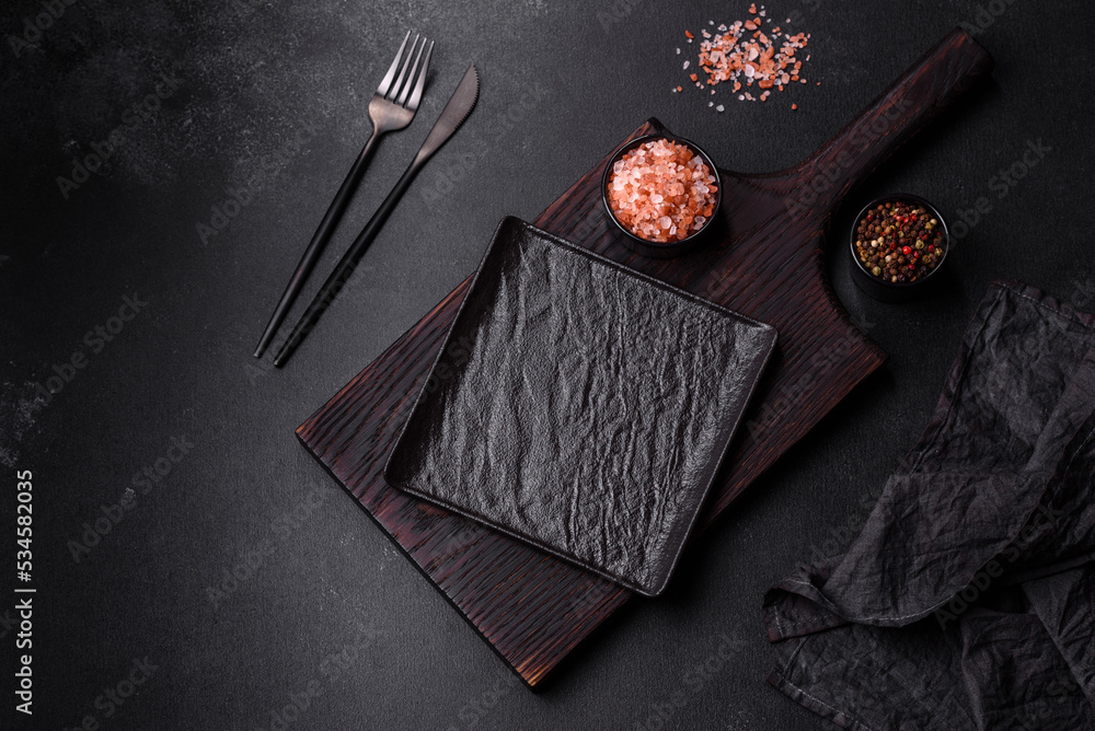 Fototapeta premium Empty black plate over dark stone background with free space. Top view