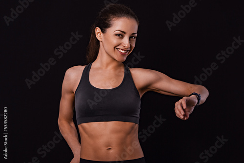 Happy smiling fit healthy fitness woman in bra top clothing looking on sporty watches what time is it now on black background with empty copy space. Closeup