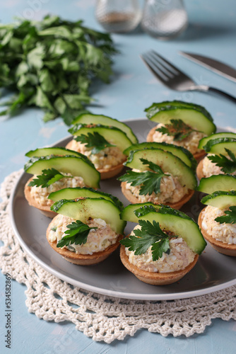Tartlets with cod liver, egg, garnished with cucumber and parsley on plate on blue background