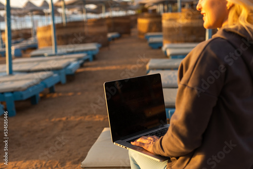 Woman sitting with laptop on the summer beach at sunset.