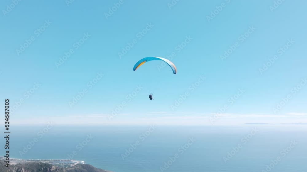 Man with instructor flies with paraglide 4k, slow motion up in the air, cinematic aerial drone footage above Malibu USA. Extreme paraglider flying against a clear blue sky, sunbeam shines into camera Man with instructor flies with paraglide 4k, slow motion up in the air, cinematic aerial drone footage above Malibu USA. Extreme paraglider flying against a clear blue sky, sunbeam shines into camera