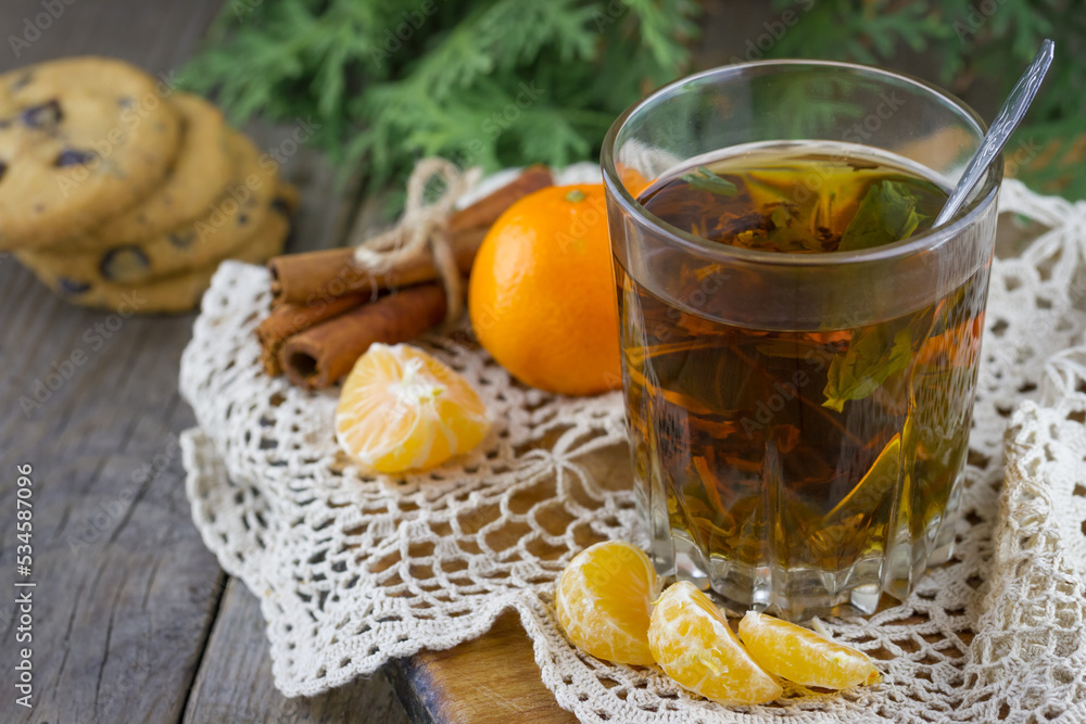 Christmas (New Year) composition. Glass cup of tea with mint, tangerine slices, cinnamon sticks, chocolate chip cookies and thuja branches on wooden background Christmas (New Year) composition. Glass cup of tea with mint, tangerine slices, cinnamon sticks, chocolate chip cookies and thuja branches on wooden background
