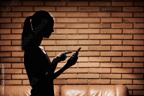 silhouette of young woman texting looking at smart phone indoors 