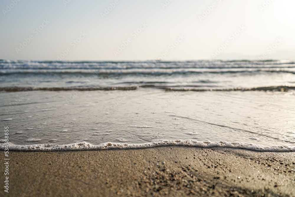 foamy bubble waves crashing gently from the sea to the beach at sunset, selective focus