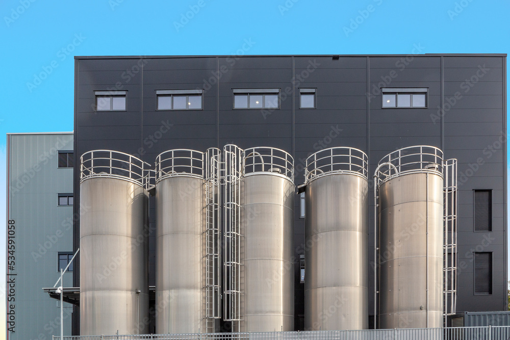 chrome silos in front of generic grey wall of a plant