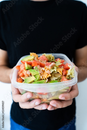 Hands holding a healthy mediterranean pasta salad tupperware