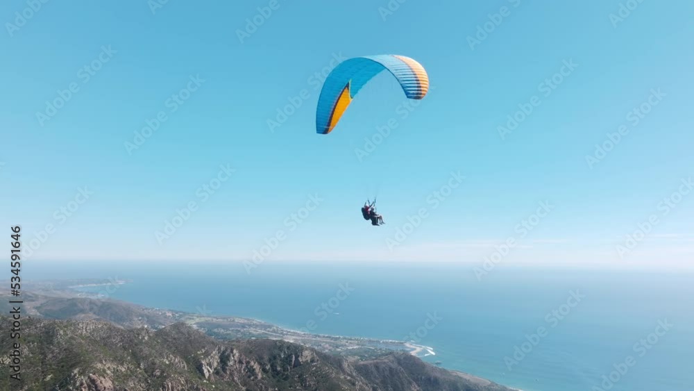 Slow motion up in the air, cinematic aerial drone footage above Malibu USA. Extreme paraglider flying against a clear blue sky, sunbeam shines into camera. Man with instructor flies with paraglide 4k Slow motion up in the air, cinematic aerial drone footage above Malibu USA. Extreme paraglider flying against a clear blue sky, sunbeam shines into camera. Man with instructor flies with paraglide 4k