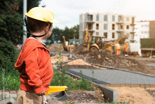 Child with excavator near construction site, dreams to be an engineer. Little builder. Education, and imagination, purposefulness concept