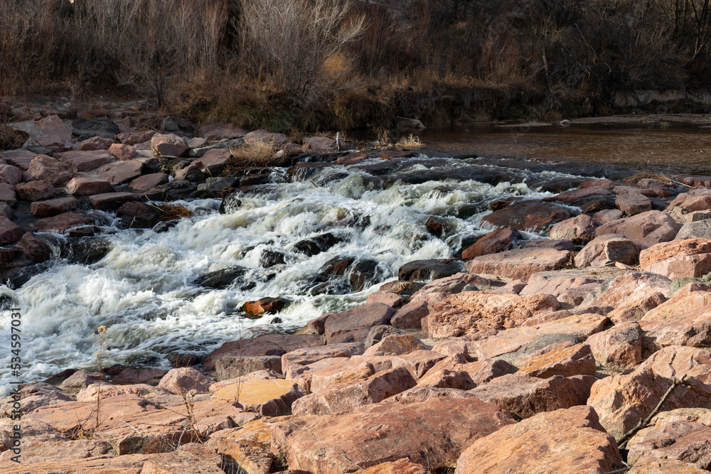 Water swiftly cascading over rocks in a stream, winter landscape in sun and shadows, horizontal aspect Water swiftly cascading over rocks in a stream, winter landscape in sun and shadows, horizontal aspect