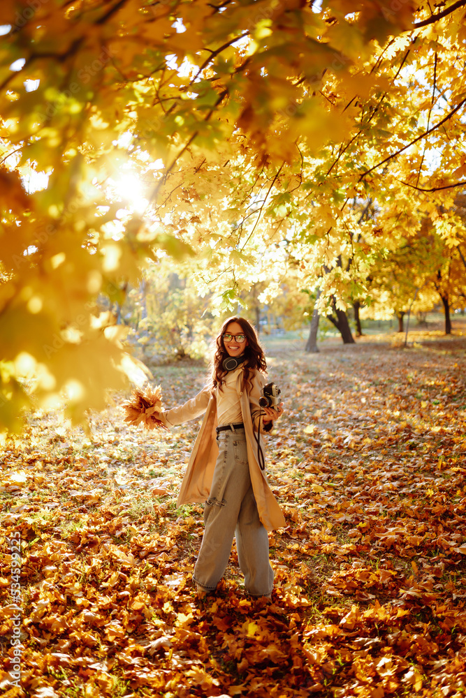 Young woman taking pictures in the autumn forest. Lady Walking In Fall Park With Yellow Foliage. Young woman taking pictures in the autumn forest. Lady Walking In Fall Park With Yellow Foliage.